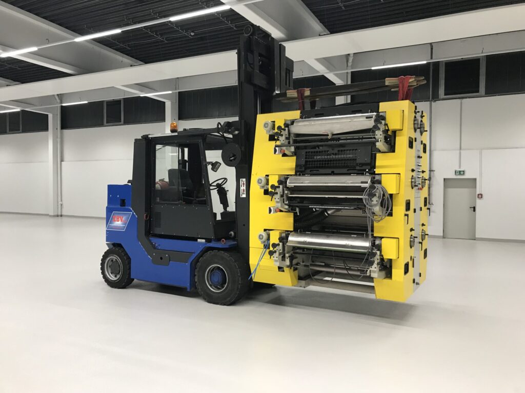 Gabelstapler hebt große gelbe Industriemaschine in hellem Lagerraum.