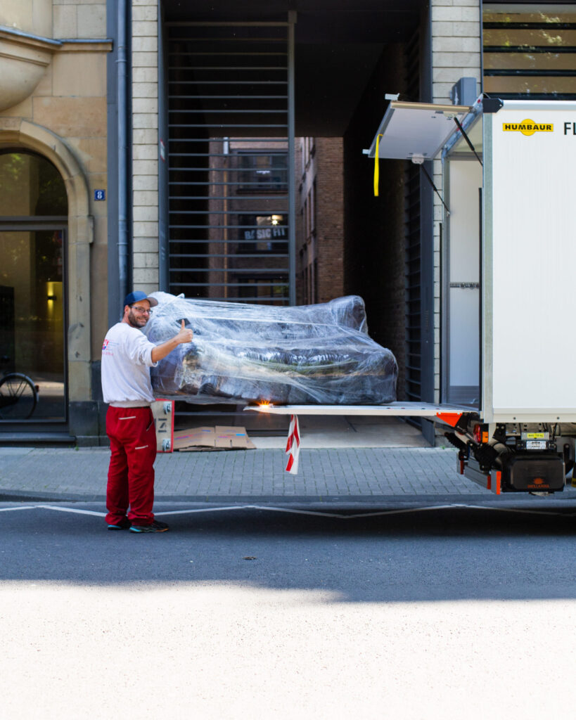 Ein Mitarbeiter hält ein eingepacktes Sofa auf einer LKW Laderampe