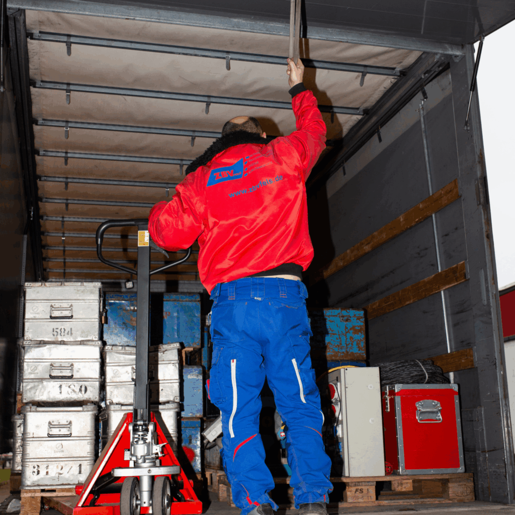 Zuverlässige Betriebsverlagerung von ZBV Fels: Mitarbeiter sichert Fracht im LKW mit Hubwagen und stapelbaren Metallkisten – ideal für Umzüge, Projektlogistik und Maschinenumzüge.