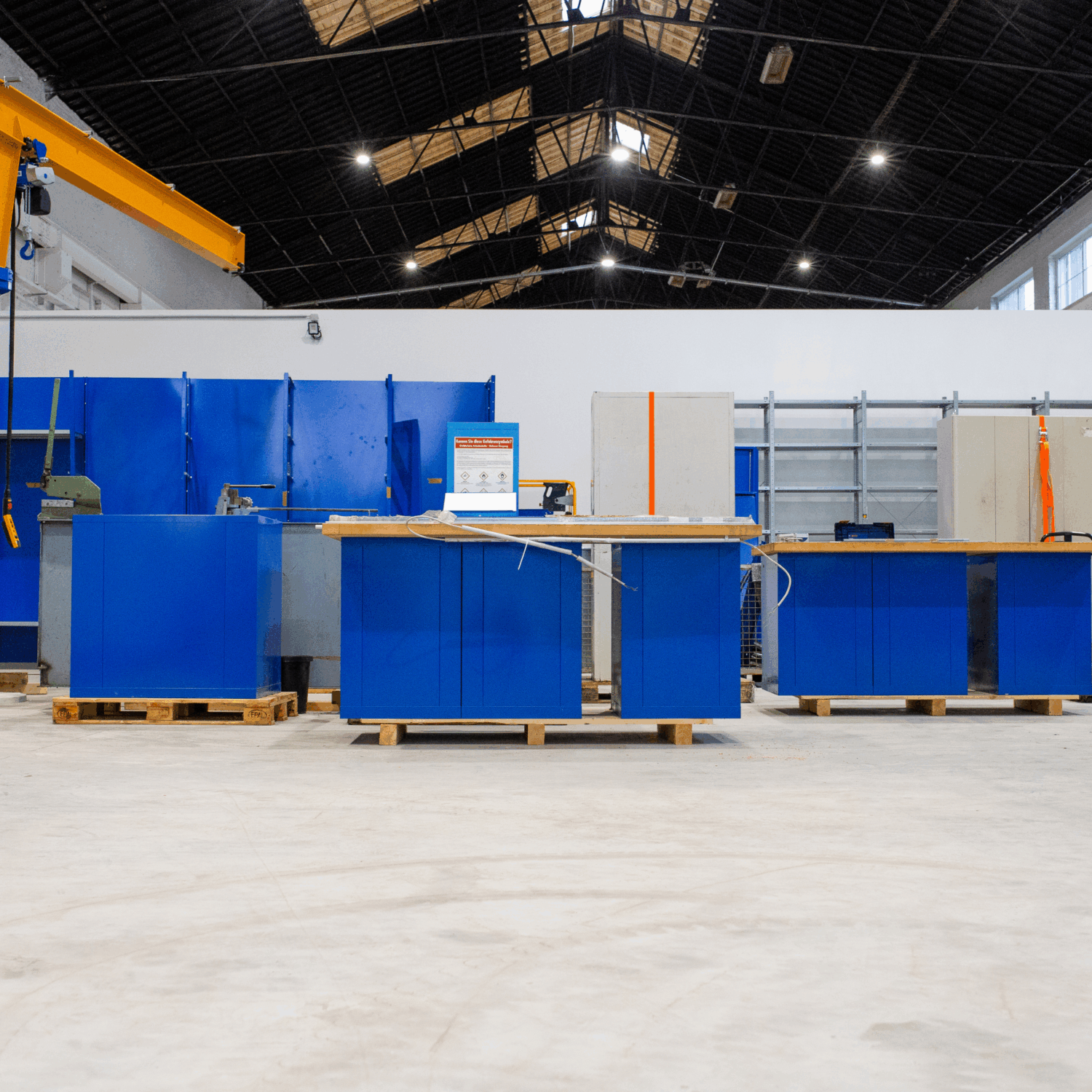 Industrielle Werkhalle mit mehreren blauen Werkbänken auf Paletten, sauberem Betonboden und hoher Hallendecke – vorbereiteter Arbeitsplatz für Maschinen- oder Montagearbeiten bei Lagerumzüge.