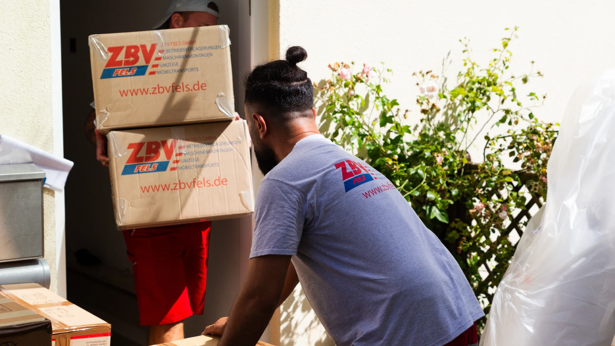 Zwei Männer tragen Kartons mit ZBV-Logo beim Umzug.