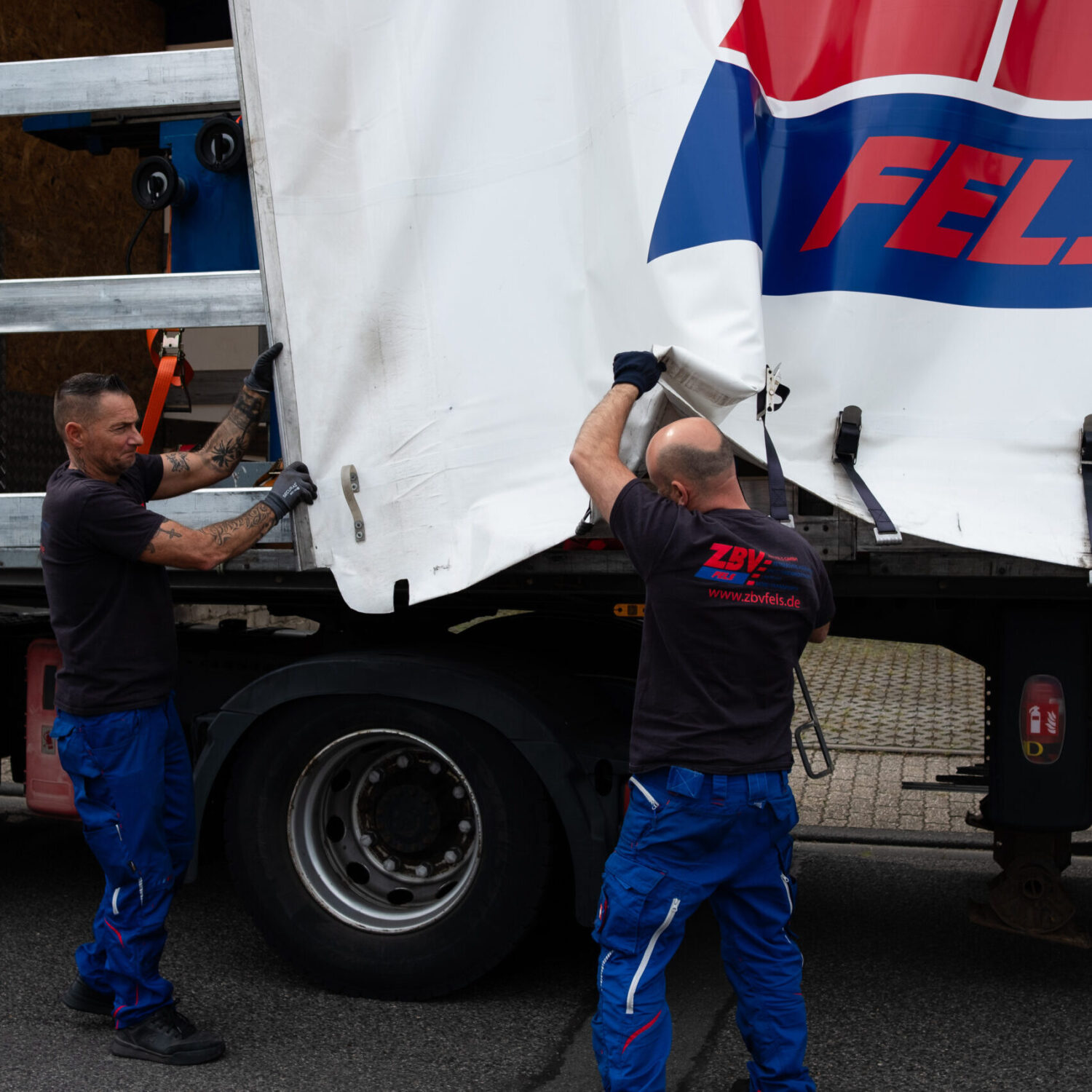 Zwei Mitarbeiter öffnen Plane eines LKW-Aufliegers